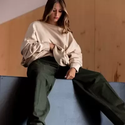 Mulher vestindo sweat bege e calças verde-escuro sentada num banco cinzento