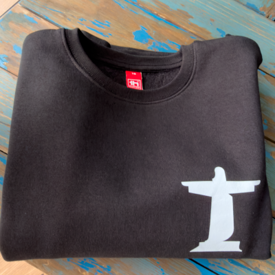 Sweatshirt preta com estampa do Cristo Redentor branca dobrada sobre mesa de madeira azul desgastada