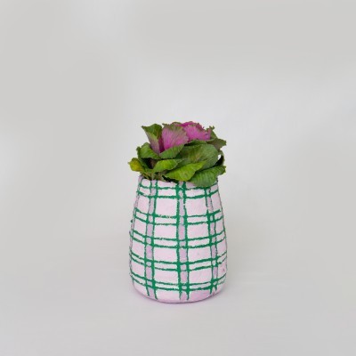 Vaso tecido rosa com riscas verdes e plantas artificiais cor de rosa em fundo branco