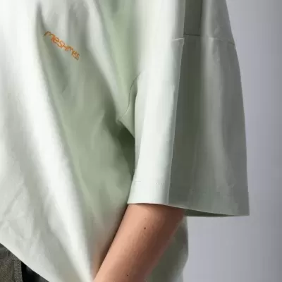 Camiseta branca oversize com texto laranja mesamis perto do peito