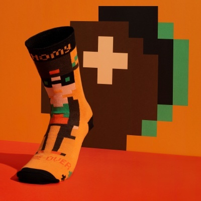 Meia colorida com padrão pixelado de personagem e texto 'GAME OVER' sobre fundo laranja
