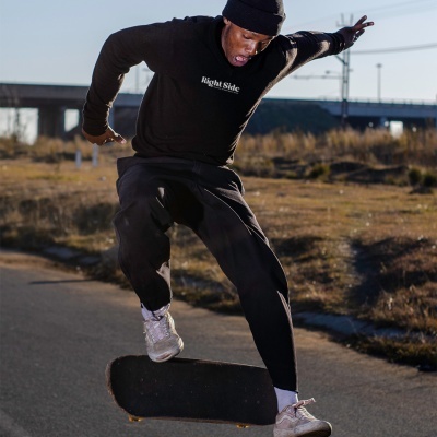 Pessoa a andar de skate com sweatshirt preta 'Right Side' e calças pretas numa estrada ao ar livre