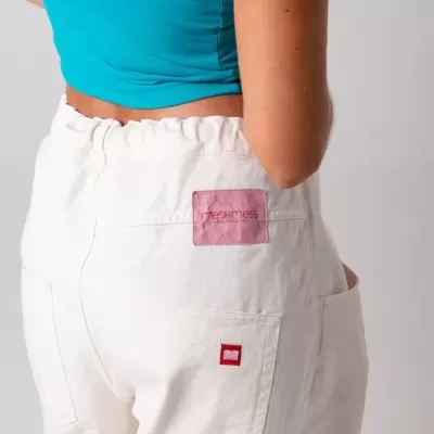 Calças brancas com etiquetas rosa e vermelha usadas por mulher com top azul