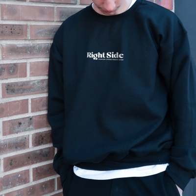 Sweatshirt preta com texto branco 'Right Side FASHION STREETWEAR SUPPLY' contra parede de tijolos vermelhos