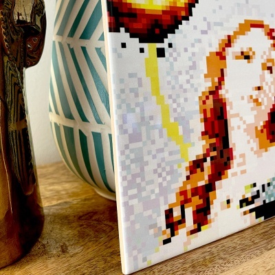 Escultura dourada, vaso geométrico azul e branco, imagem pixelada colorida, sobre mesa de madeira.