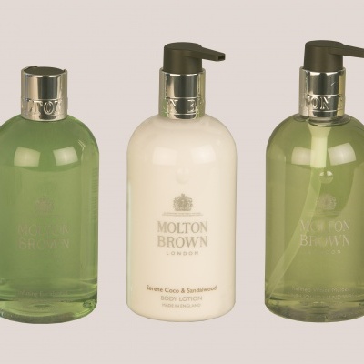 Três frascos de produtos Molton Brown com dispensador em fundo neutro