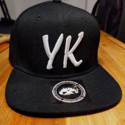 Boné preto com letra YK branca e etiqueta com desenho de peixe
