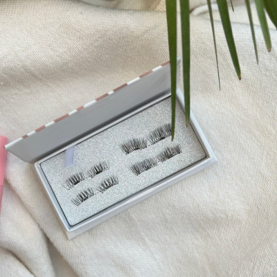 Caixa branca com cílios postiços sobre tecido bege perto de bambu e folhas verdes