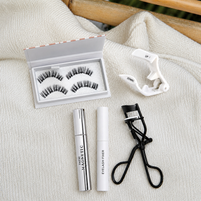 Conjunto de cosméticos e acessórios para pestanas sobre tecido branco.