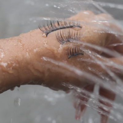 Mão molhada segura pestanas postiços pretos sob água corrente.