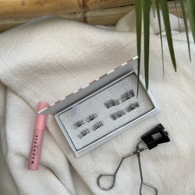 Conjunto de pestanas magnéticas com caixa, tubo rosa e curvador sobre tecido branco