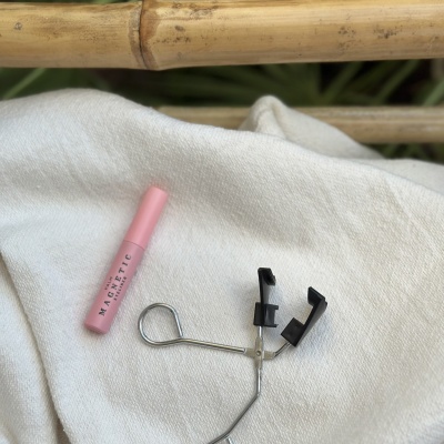 Curvex de metal com almofadas pretas e tubo rosa de rímel MAGNETIC sobre tecido branco e bambu