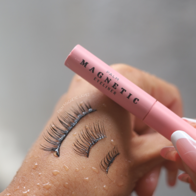 Eyeliner magnético rosa sendo segurado sobre mão com pestanas magnéticas coladas e gotas de água