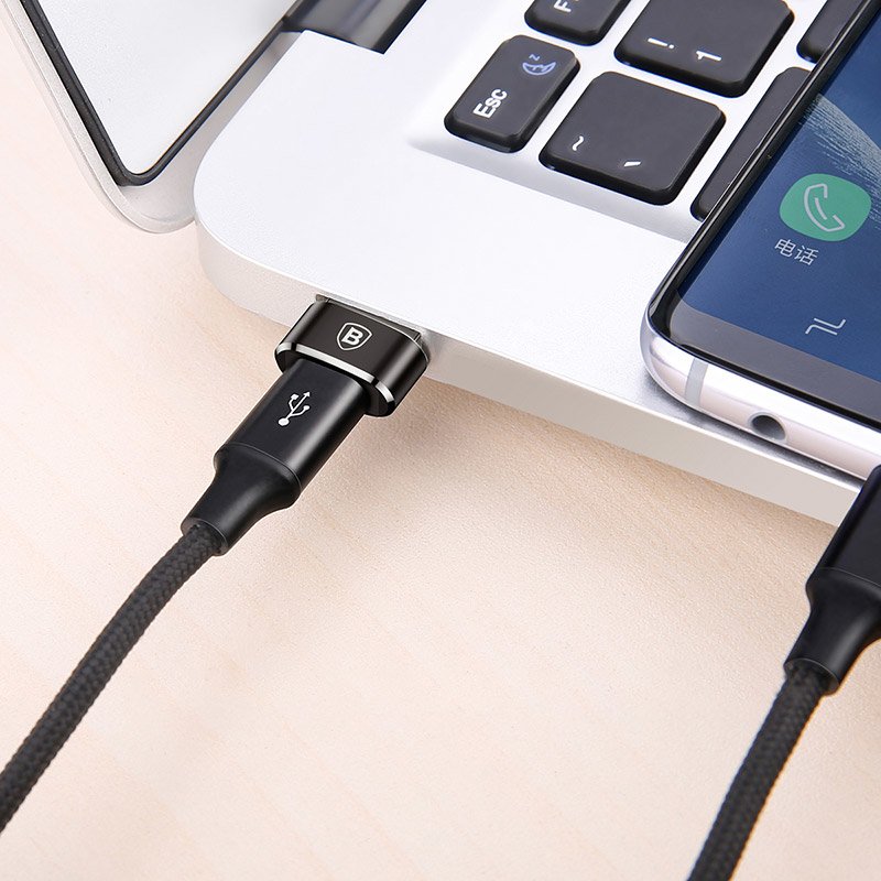 Cabo USB preto a ligar smartphone a portátil prateado sobre mesa clara