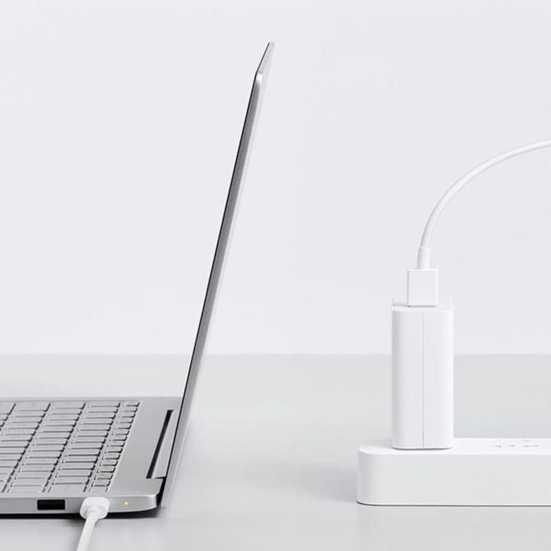 Notebook cinzento claro ligado a uma tomada e régua de energia brancas