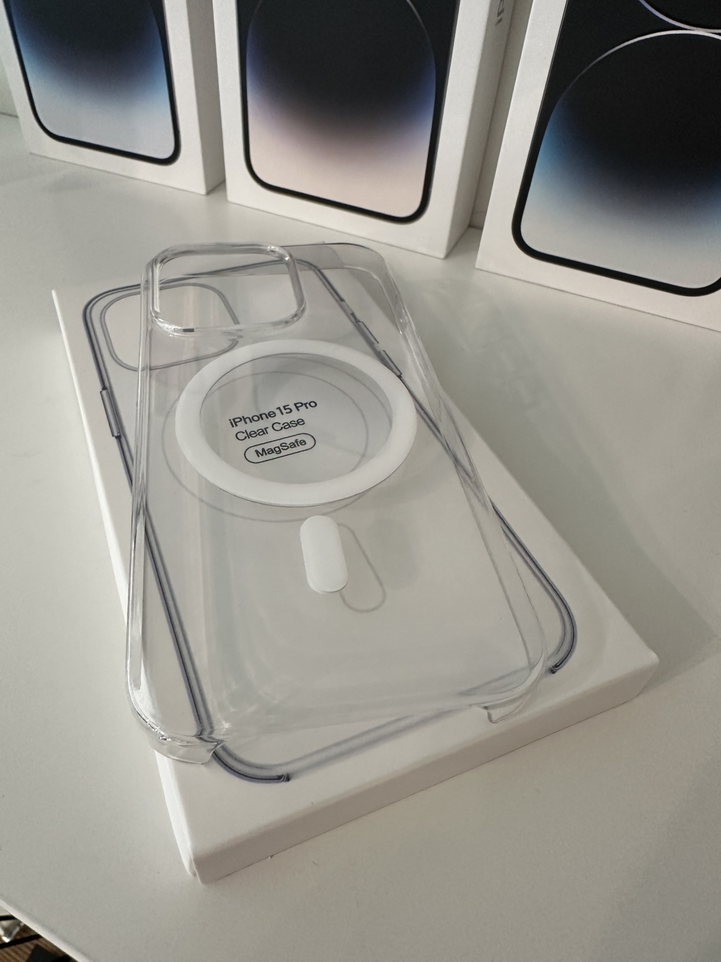 Capa Transparente MagSafe Premium para iPhone 15 Pro Max Capa transparente para iPhone 15 Pro com MagSafe sobre caixa branca e três caixas de iPhone ao fundo
