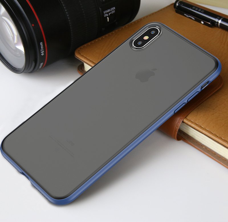 iPhone X/XS Capa Transparente Mate iPaky Cucorolis Smartphone Apple iPhone com capa azul sobre superfície branca, junto a lente de câmara preta e caderno castanho.