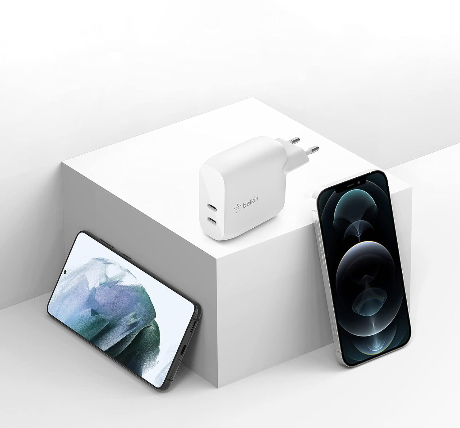 Carregador / Adaptador de corrente Belkin 40W BoostCharge Dual Carregador Belkin branco com duas portas USB junto a dois telemóveis sobre cubo branco