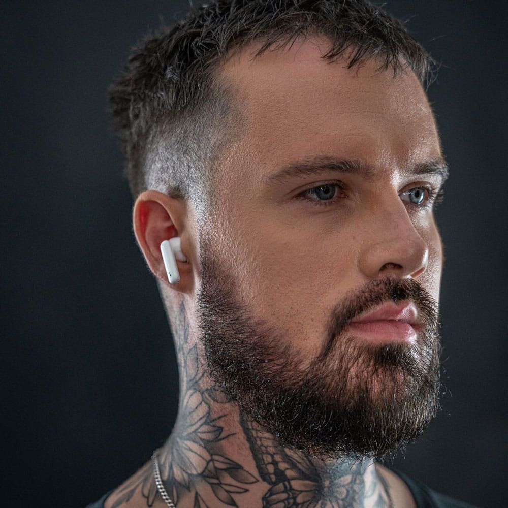 Auriculares 3mk Hardy LifePods Pro™ ANC - Branco Homem com auricular branco sem fios no ouvido direito e tatuagens no pescoço