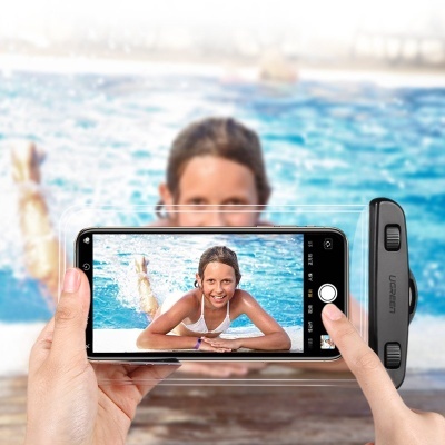 Pessoa a fotografar menina sorridente na piscina com smartphone preto e dispositivo UGREEN na lateral.