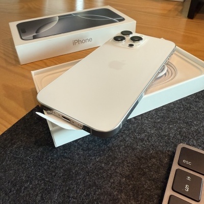 iPhone branco com três câmaras na caixa aberta sobre mesa de madeira e teclado próximo