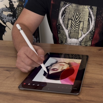 Pessoa desenhando numa tablet digital com caneta branca numa mesa de madeira