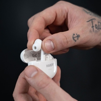 Auriculares sem fios brancos em estojo branco com a marca HARDY, mãos segurando os auriculares
