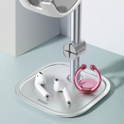 Suporte metálico prateado para telemóvel com base onde estão dois auriculares brancos e um acessório cor-de-rosa