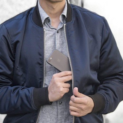 Homem a vestir casaco bomber azul escuro a segurar um smartphone preto