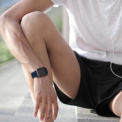 Relógio inteligente com bracelete azul e preto no pulso esquerdo de uma pessoa vestida com t-shirt branca e calções pretos.