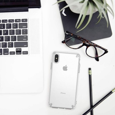 Mesa branca com computador portátil, telemóvel, óculos, lápis, caderno e planta