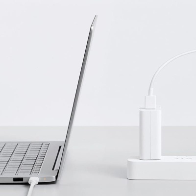 Notebook cinzento claro ligado a uma tomada e régua de energia brancas