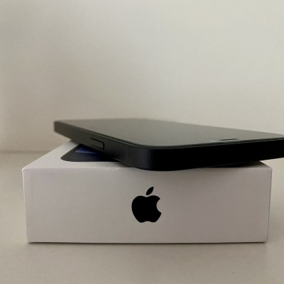 Smartphone preto sobre caixa branca com logotipo da Apple junto a um vaso de planta.