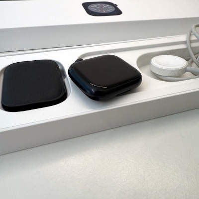 Relógio inteligente negro com pulseira preta dentro de caixa branca com carregador wireless branco