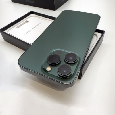 Smartphone iPhone verde com três lentes traseiras e caixa preta com texto iPhone