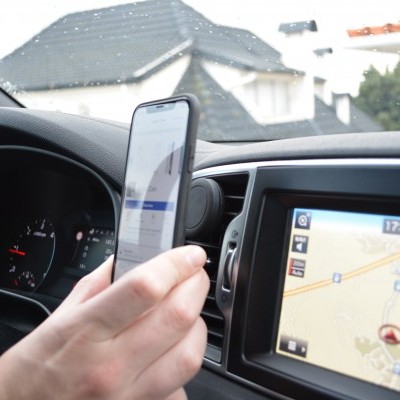 Suporte de telemóvel preto dentro de carro com telemóvel na mão e painel com GPS.