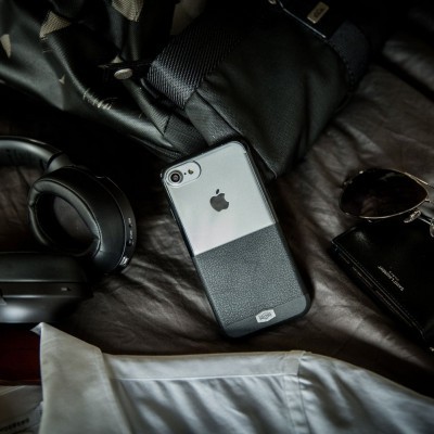 Capa para iPhone sobre superfície escura com auscultadores, óculos, carteira e camisa