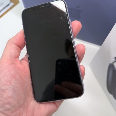 Smartphone com ecrã preto e moldura metálica prateada na mão com caixa Apple atrás