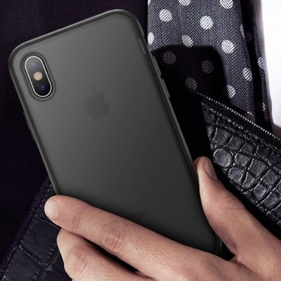 Smartphone Apple iPhone com capa preta fosca, duas câmaras traseiras, segurado por mão com fundo de pele de crocodilo e tecido azul com bolinhas