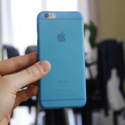 iPhone com capa azul segurado por uma mão, ambiente interior desfocado