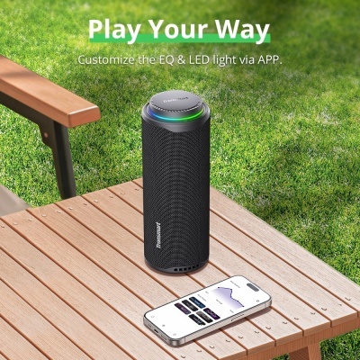 Coluna portátil preta Tronsmart com LED e smartphone sobre mesa de madeira no exterior