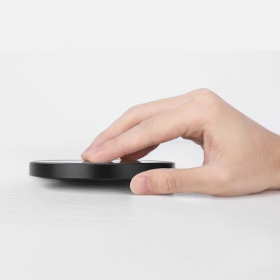 Carregador wireless preto redondo com mão.