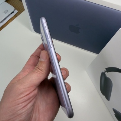 Pessoa a segurar iPhone prateado com caixas de MacBook Neo e auscultadores ao fundo