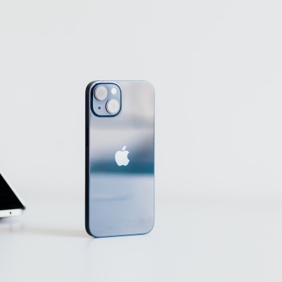 iPhone azul metálico com logótipo da Apple numa mesa branca ao lado de portátil