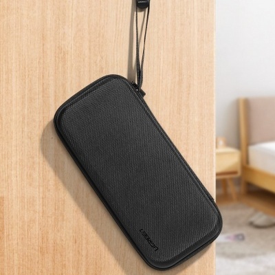 Bolsa preta retangular texturizada com fecho e fita pendurada em madeira clara