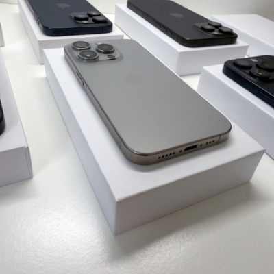 Cinco iPhones com acabamento fosco em cores preta e cinza, cada um sobre uma caixa branca