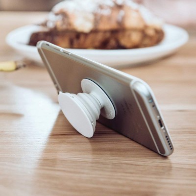 Smartphone cinzento apoiado com suporte branco tipo pop socket numa mesa de madeira