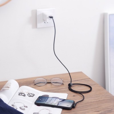 Cabo de carregamento preto ligado a telemóvel sobre mesa de madeira com óculos e revista