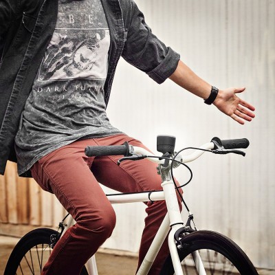 Homem jovem de camiseta cinzenta e calças castanhas sentado numa bicicleta branca