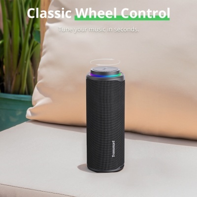 Coluna portátil preta Tronsmart com botão giratório iluminado num sofá claro junto a plantas